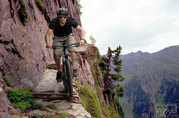 Background of same photo of male cyclist transformed to show the cyclist now riding along an extremely dangerous and precarious cliff-side track.