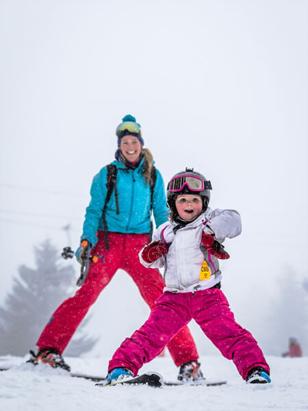 Photo of female skiers - one adult and one child - posing with a calm, flat snowfield in the background.